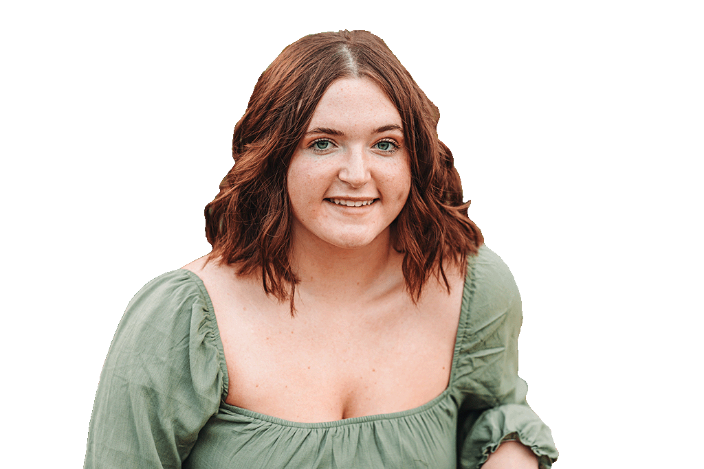 Professional portrait of a smiling woman with shoulder-length wavy auburn hair, wearing a sage green blouse, facing the camera against a transparent background.